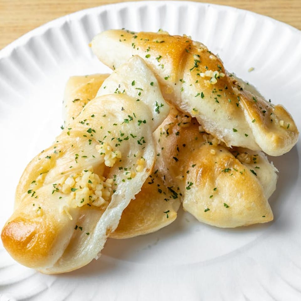 Golden brown garlic knots, topped with minced garlic and parsley, on a white paper plate.