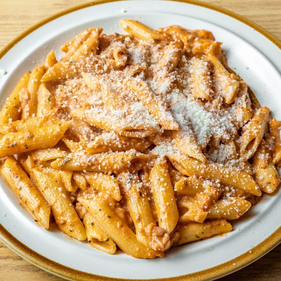 Penne pasta with creamy tomato sauce and grated Parmesan cheese on a white plate.