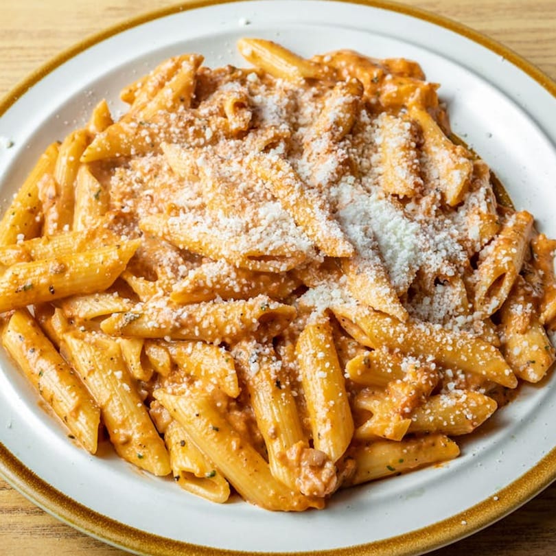 Penne pasta with creamy tomato sauce and grated Parmesan cheese on a white plate.