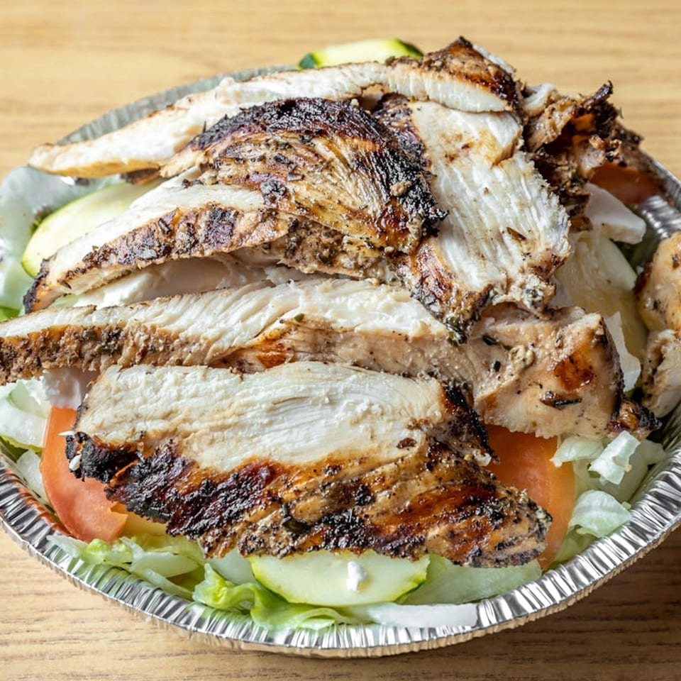 Grilled chicken slices on a bed of lettuce, tomatoes, and cucumbers in a foil container.